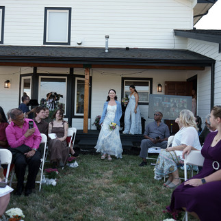 Bride walks down grassy aisle past seated guests at outdoor ceremony.