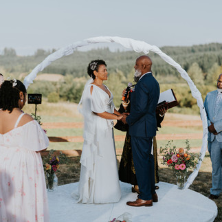 Bride and groom exchanging vows under white arch at outdoor farm wedding.