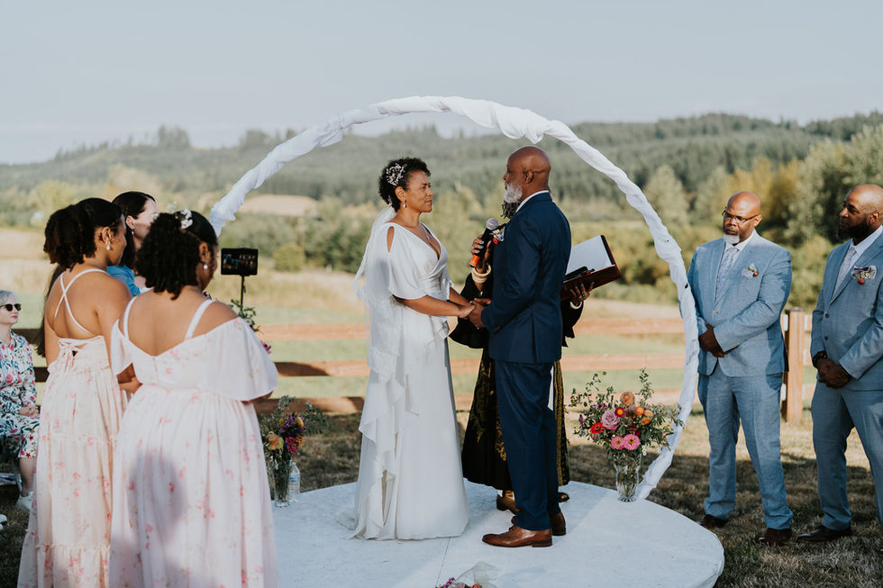 Bride and groom exchanging vows under white arch at outdoor farm wedding.