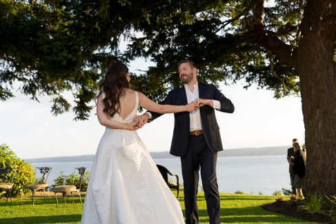 Bride and groom dancing outdoors at a wedding celebration by the water.