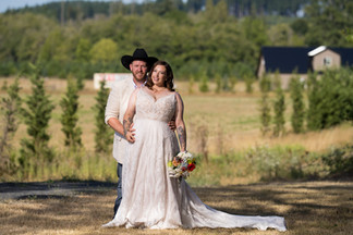 Newlyweds outdoor in summer field, groom in cowboy hat, bride with bouquet.