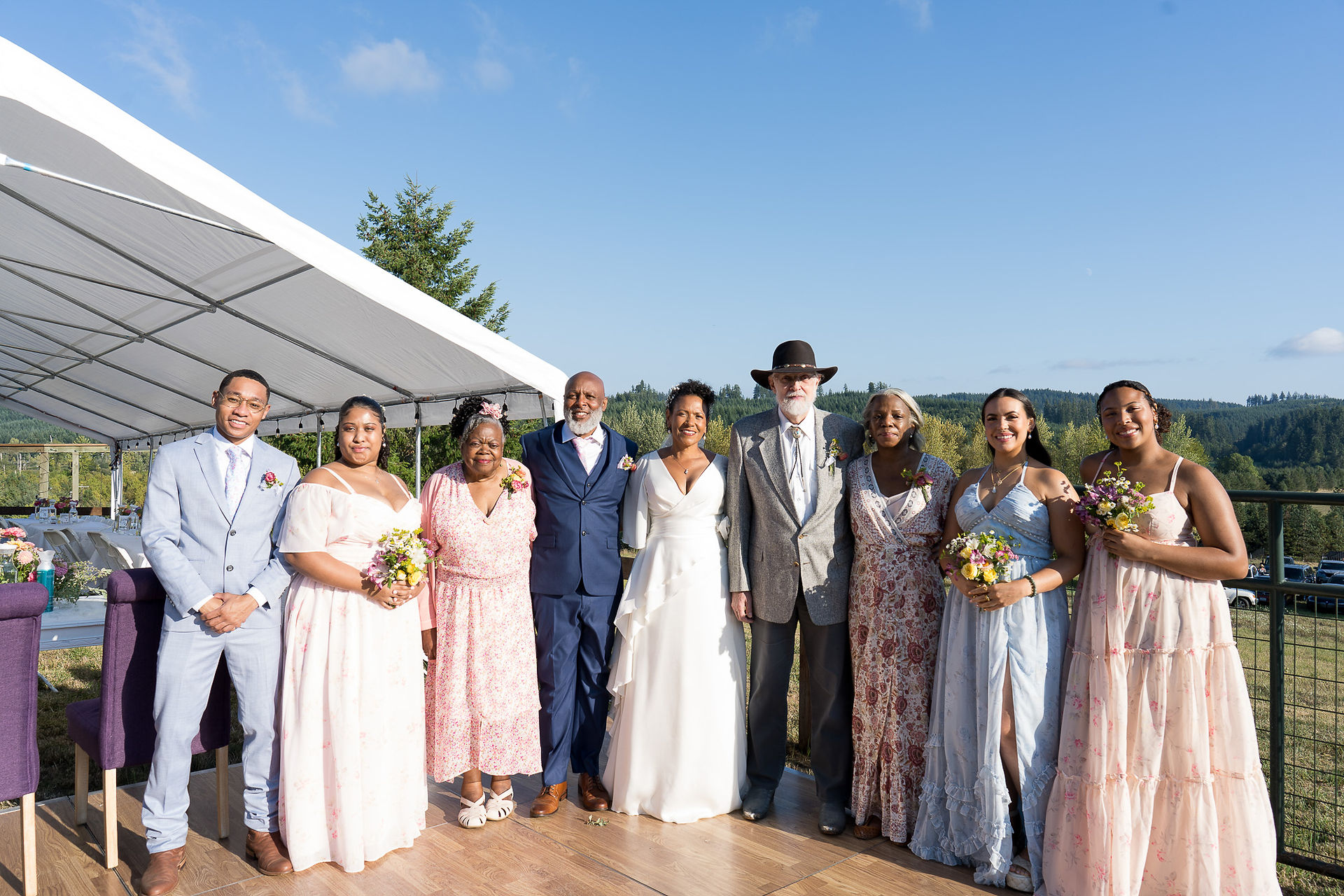 Joyful family, including bride and groom, posing at outdoor wedding.