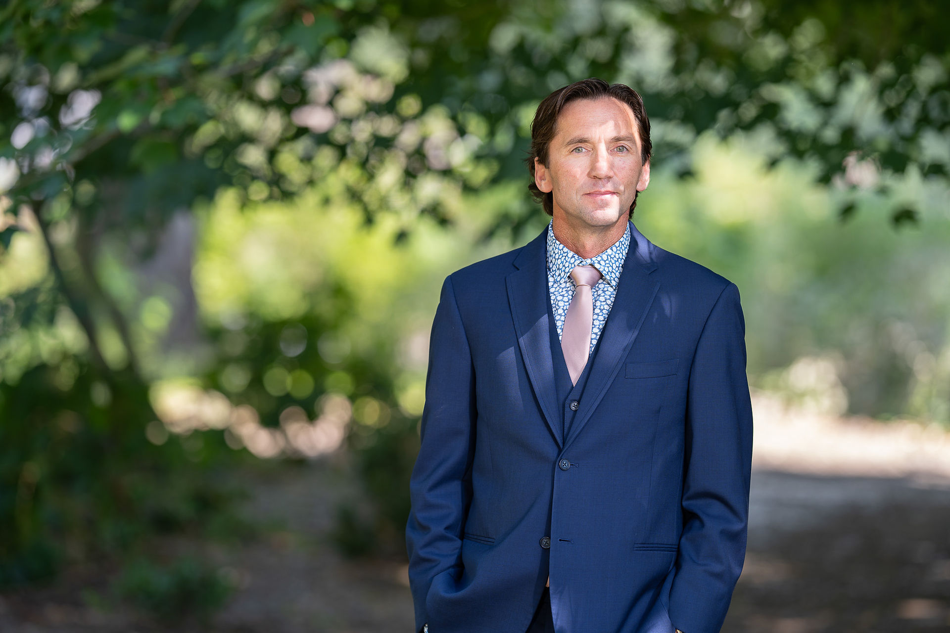 Man in blue suit and patterned tie outdoors looking thoughtful.