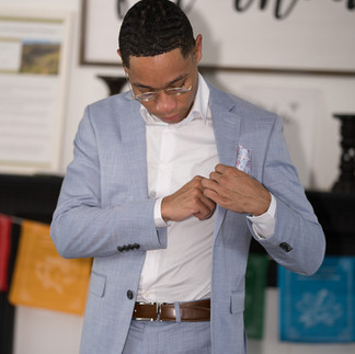 Young man in light blue suit adjusts white shirt, getting ready.