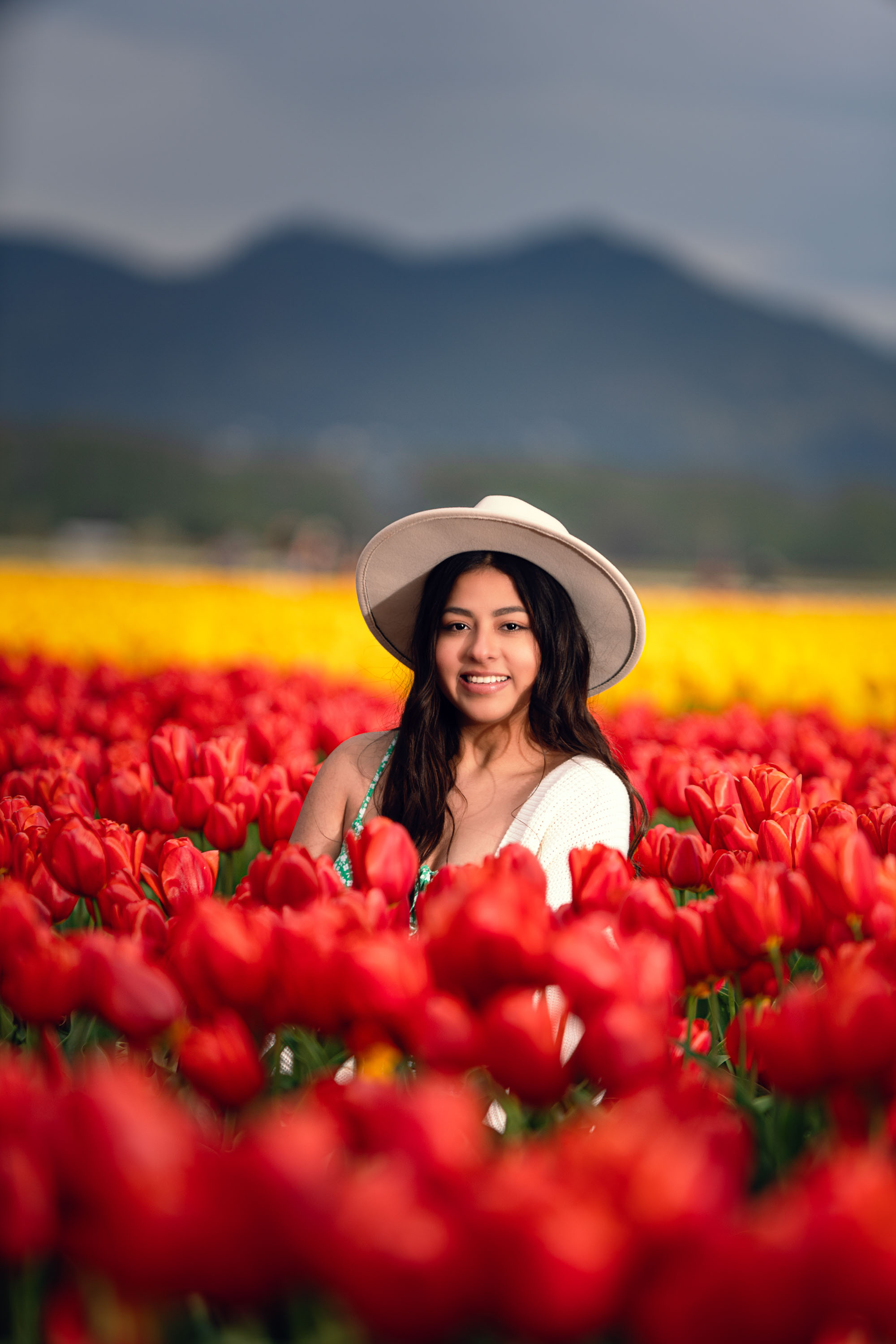 Smiling woman in white hat amidst red tulips, yellow fields, mountains, tulip festival 2026.
