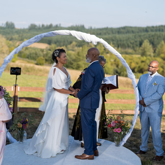 Bride and groom exchange vows under arch during intimate farm wedding.
