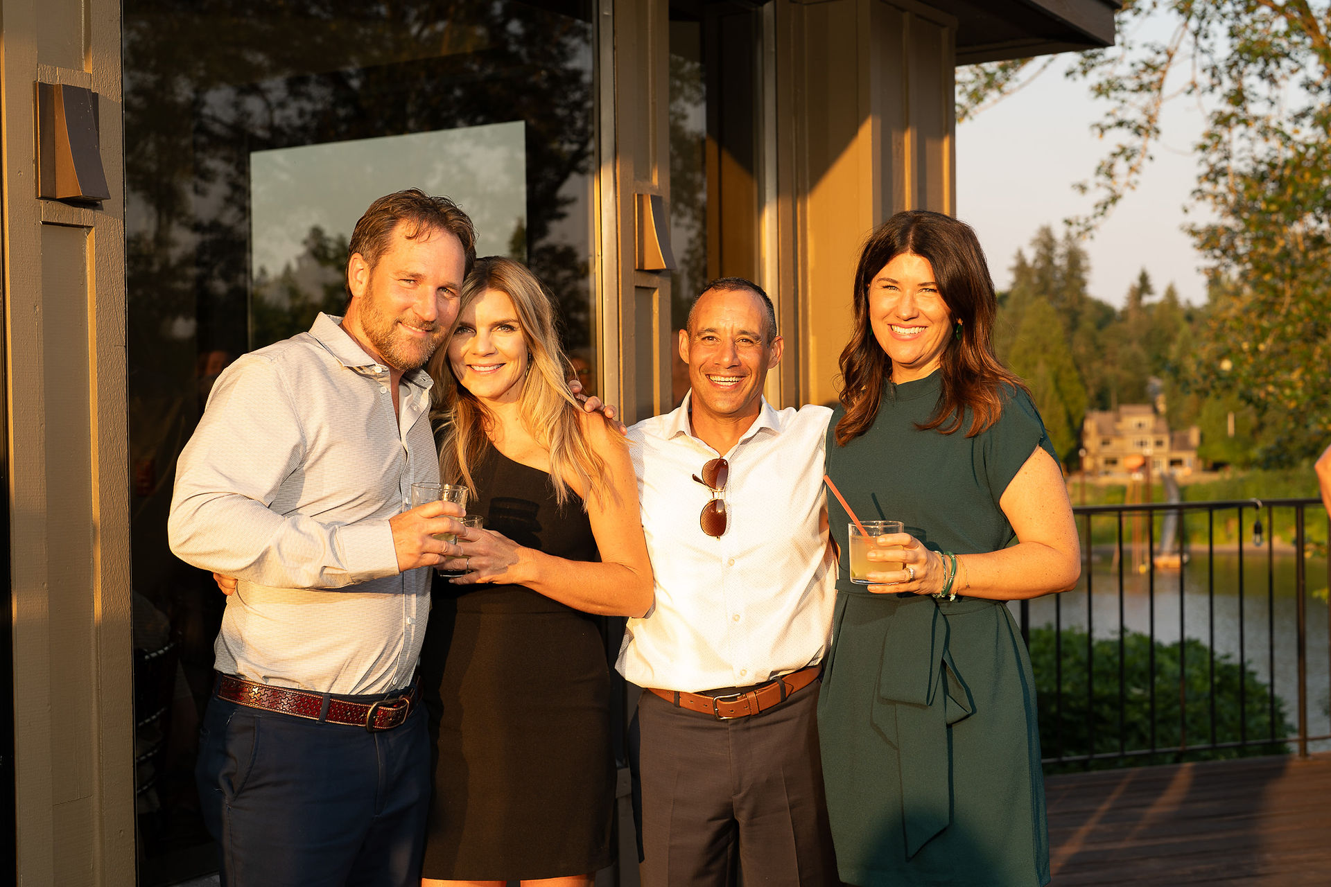 Four happy friends enjoying drinks together outdoors at sunset.