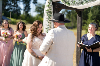Bride smiling at groom during outdoor wedding ceremony under arch.