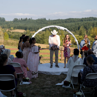 Intimate farm wedding ceremony with couple and guests under arch.