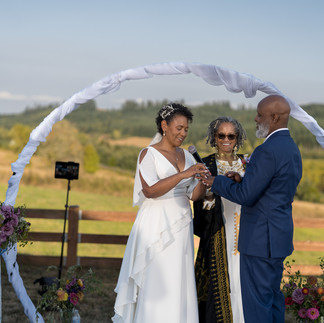 Couple exchanges rings under arch at beautiful outdoor farm wedding.
