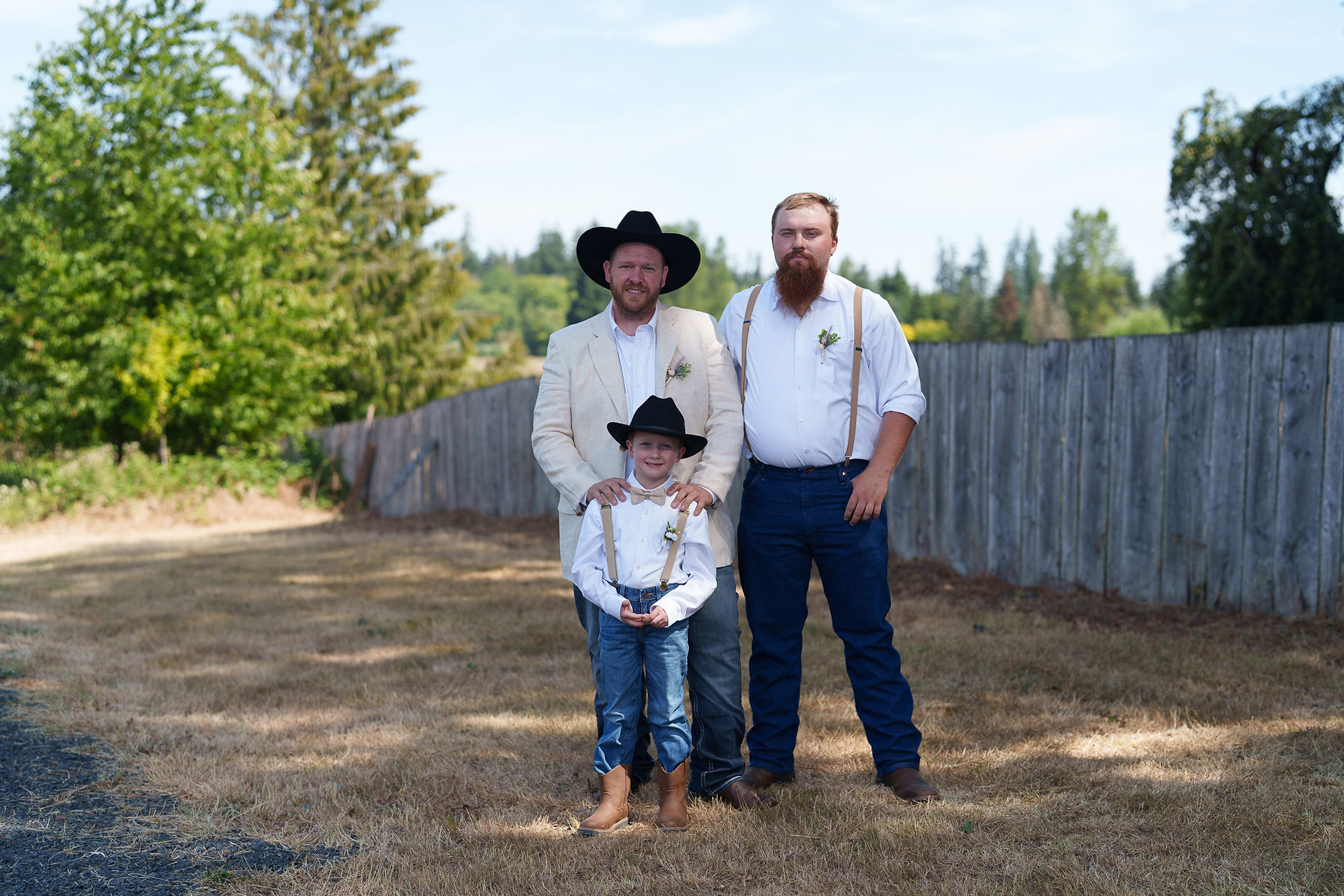 Three men and boy in hats and suspenders at outdoor wedding.