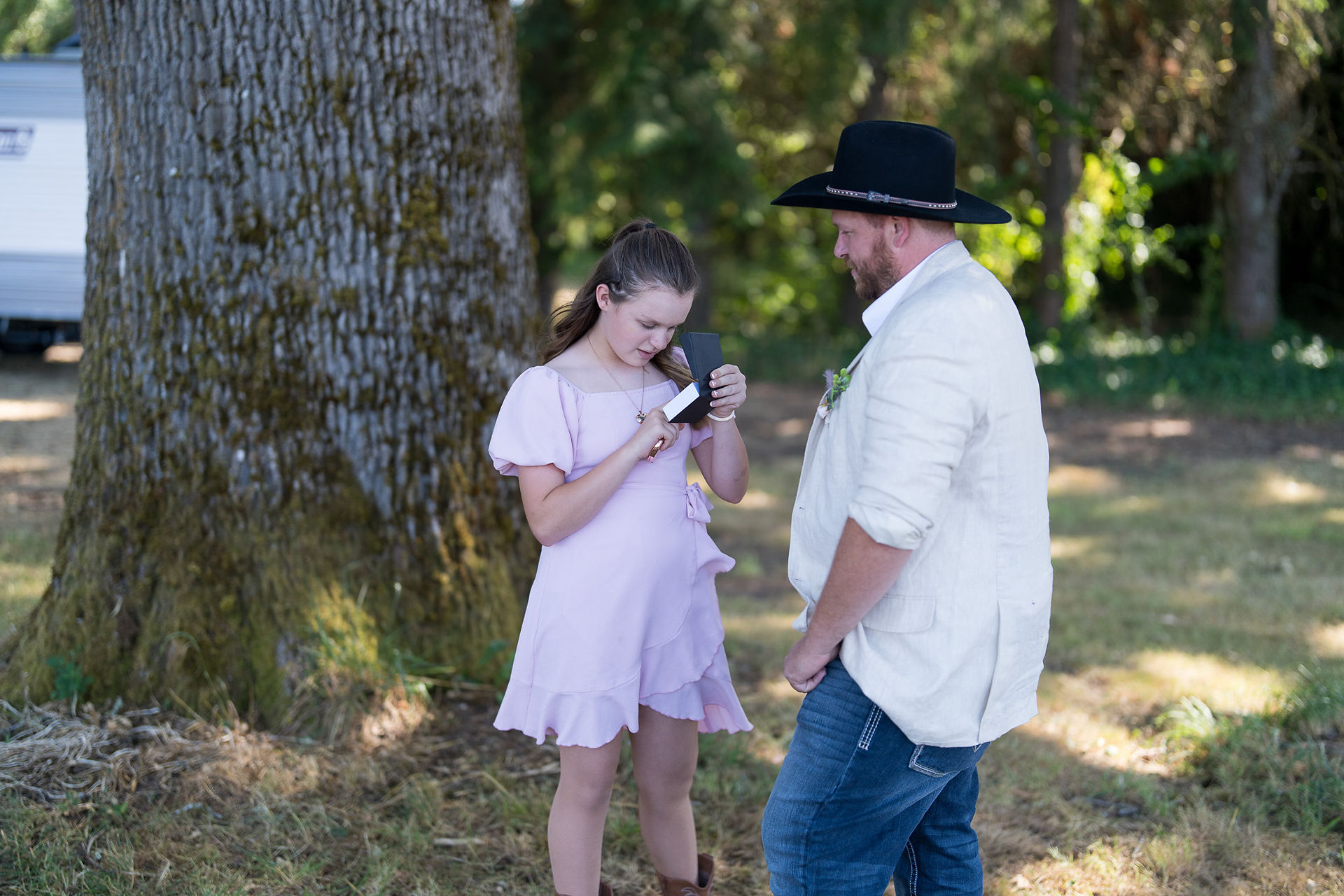 Young girl in purple dress looks at object, man watches beside her.