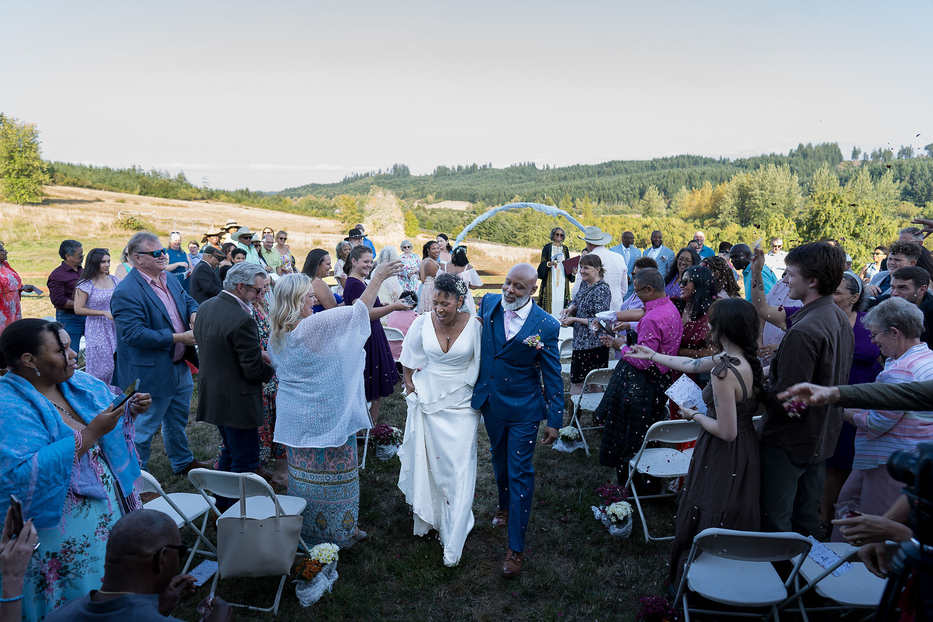 Joyful bride and groom walk through cheering guests at outdoor wedding.