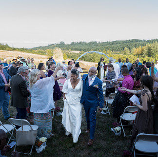 Joyful bride and groom walk through cheering guests at outdoor wedding.