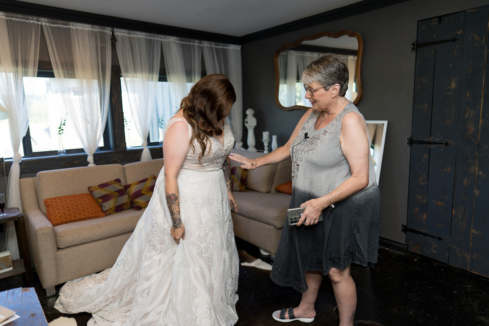 Bride getting ready, woman helping with her wedding dress indoors.