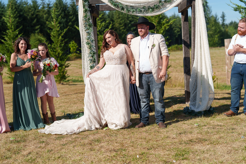 Bride and groom under rustic arch at outdoor summer wedding.