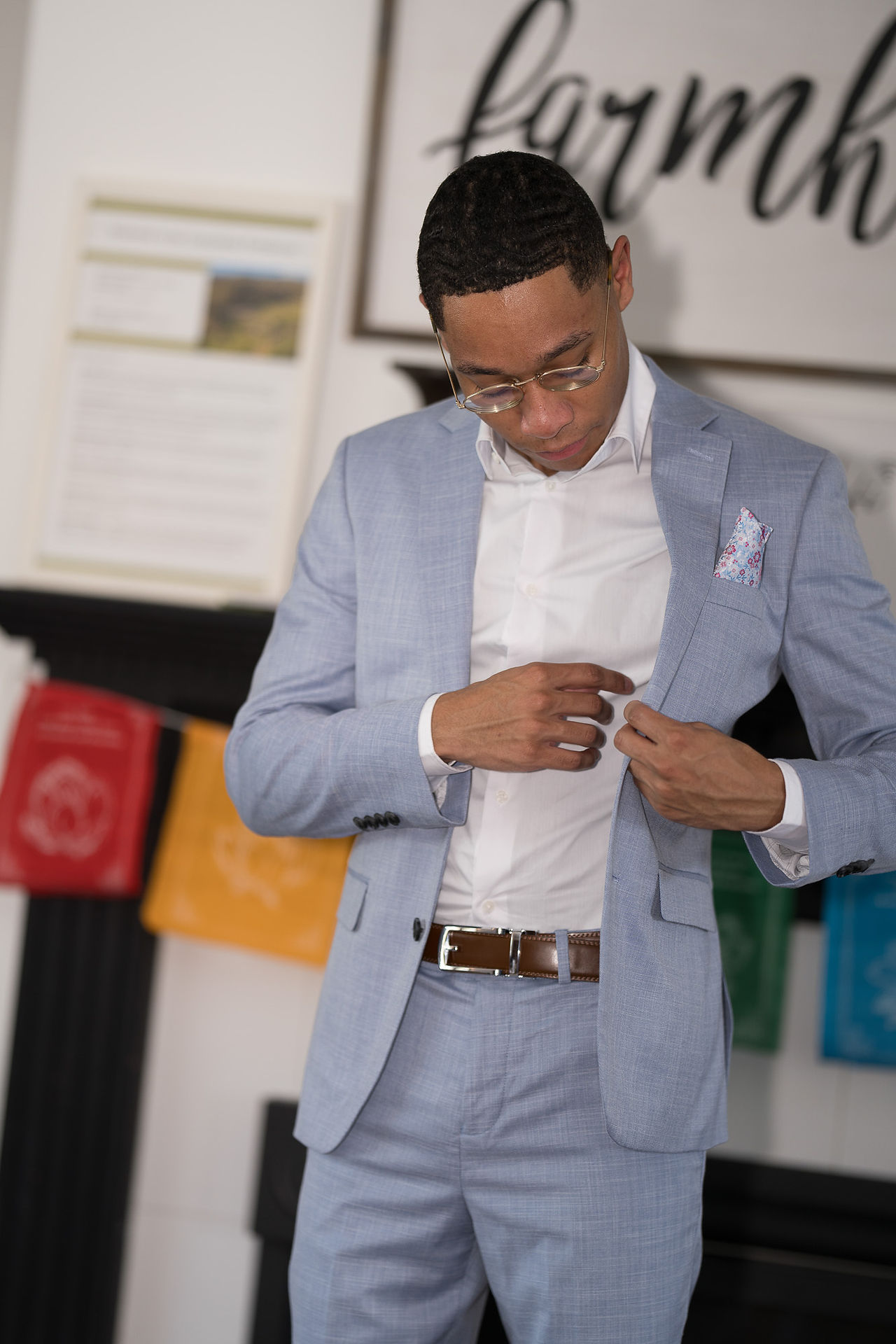 Man adjusting white shirt under light blue suit jacket indoors.