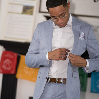 Man adjusting white shirt under light blue suit jacket indoors.