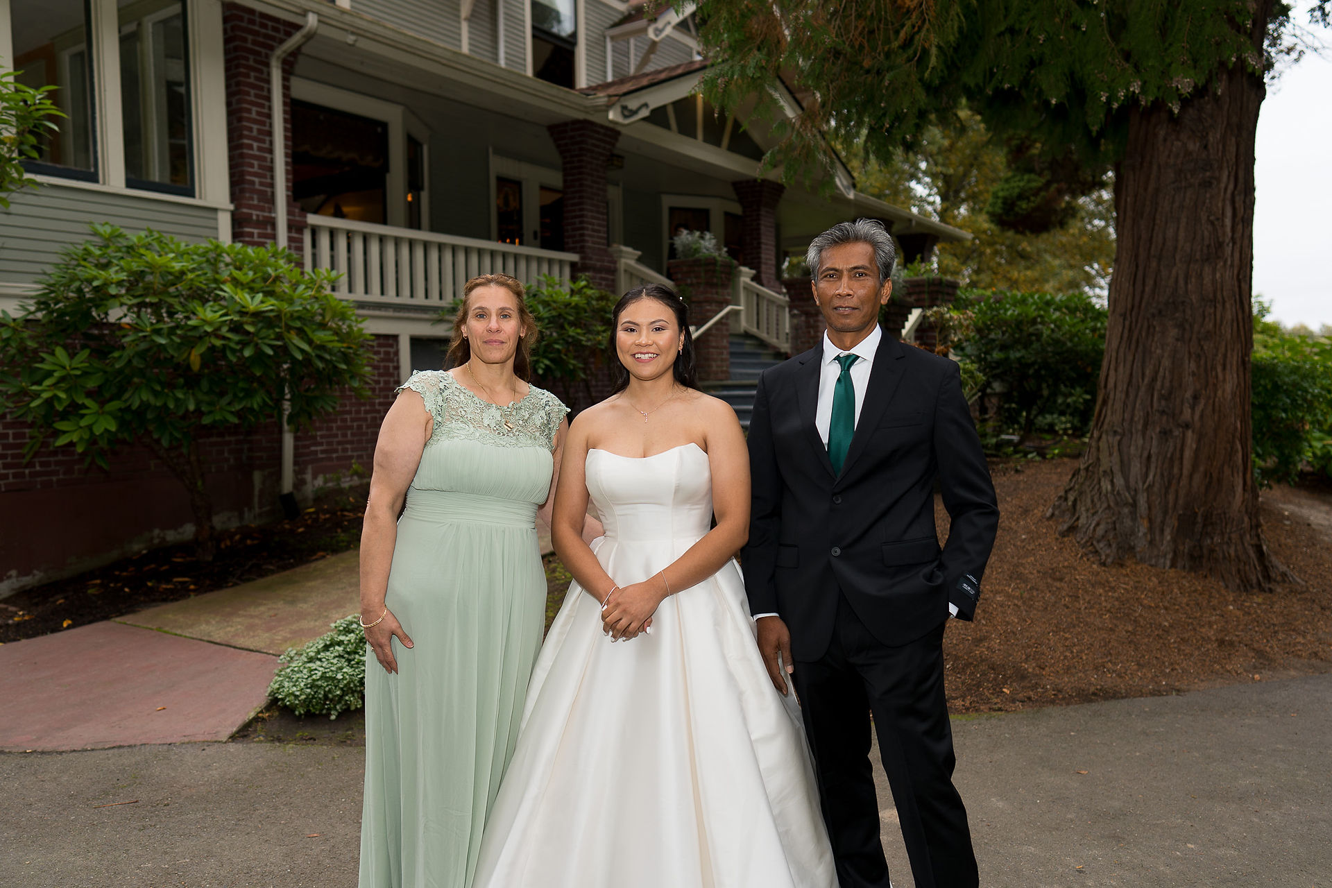 Bride, woman in green dress, man in suit posing for wedding photo.