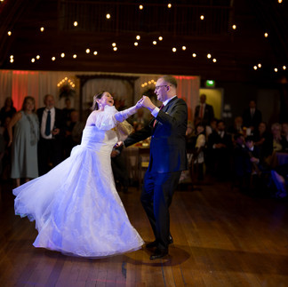 Joyful bride and groom dancing at wedding reception under warm string lights.