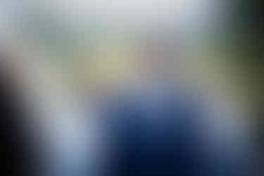 Bearded man in navy suit, pink tie, at outdoor wedding ceremony.