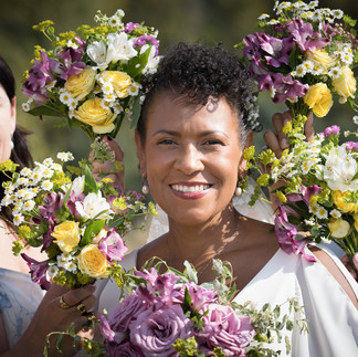 Smiling woman holding purple and yellow floral bouquet, surrounded by others.