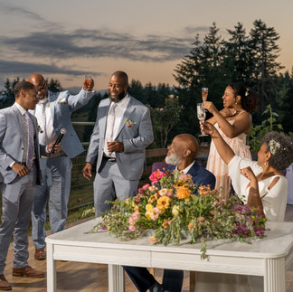 Joyful wedding guests toasting outdoors at a table with flowers.