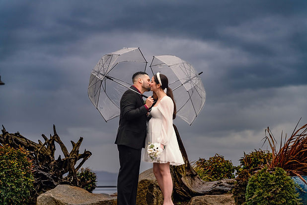 Couple kissing under umbrellas with a dark sky during engagement, PhotoYari Photography.