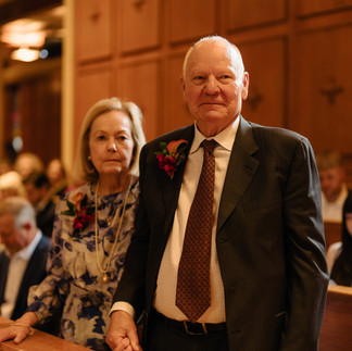 Older couple walks down aisle during wedding ceremony in chapel.