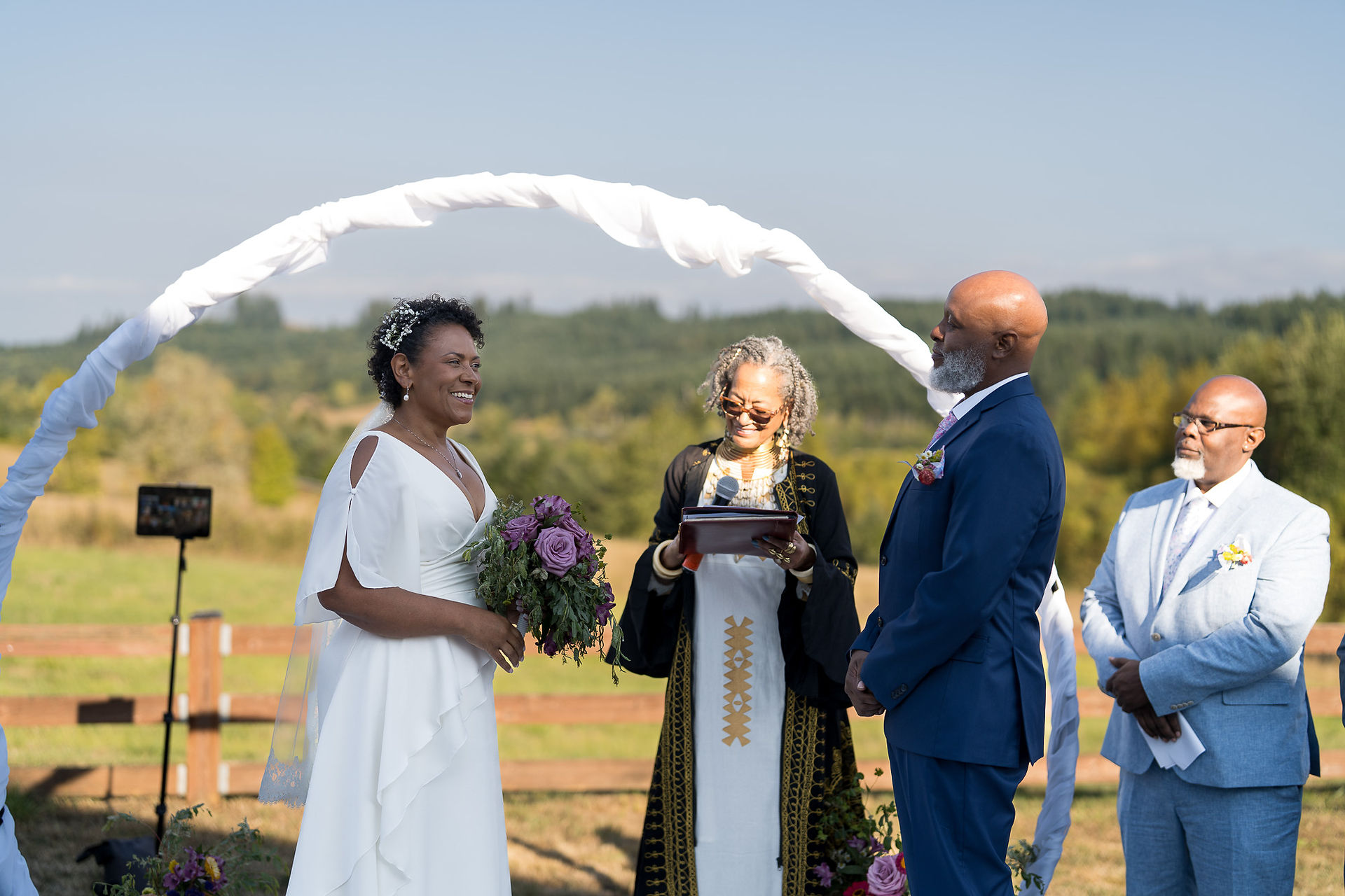 Happy couple exchanges vows with officiant at outdoor wedding ceremony.