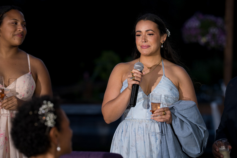 Smiling woman in blue dress gives speech, holding microphone and glass.