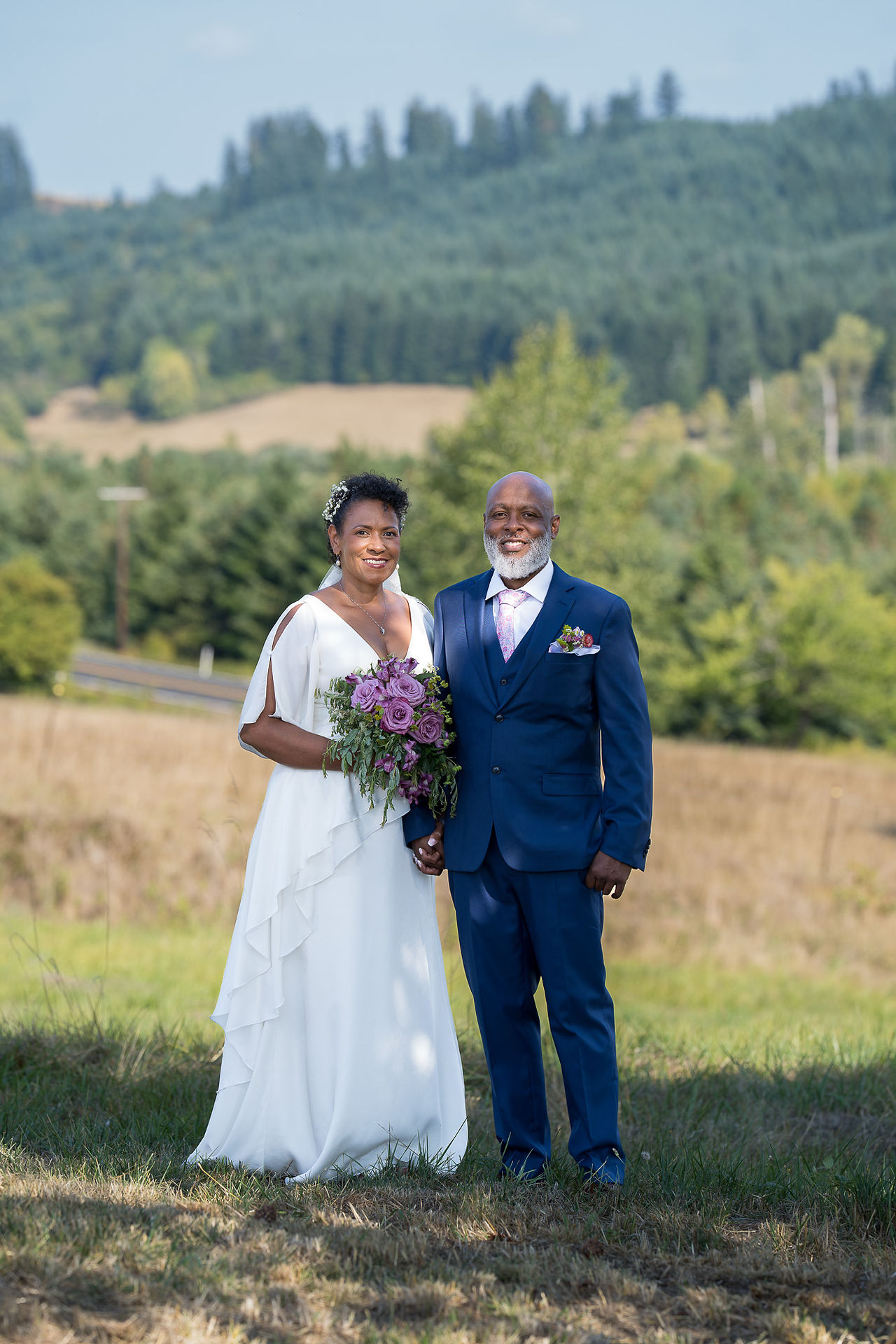 Happy Black couple holding hands at their outdoor wedding ceremony.
