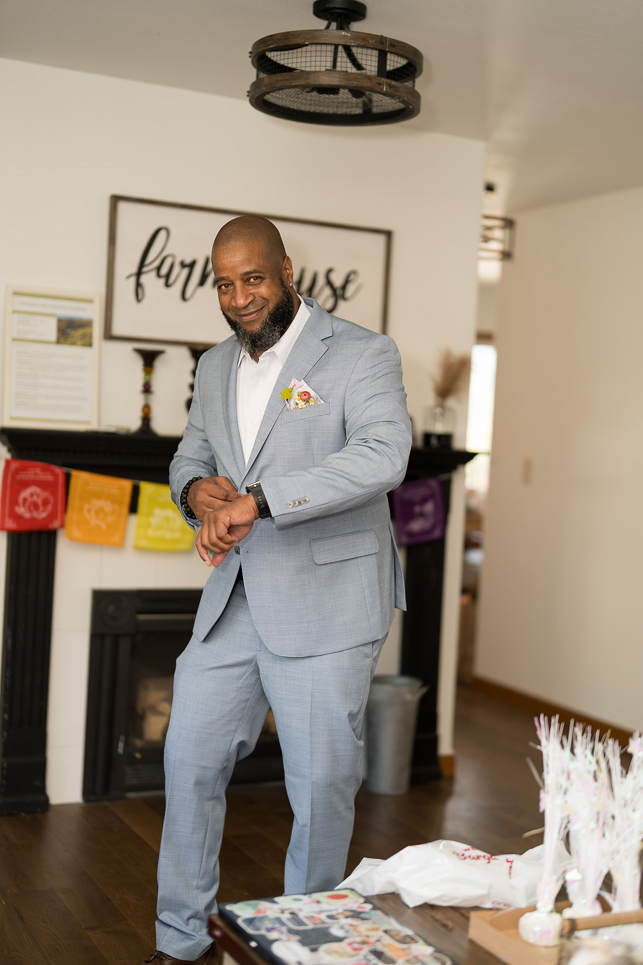 Man in light blue suit checking watch, "farmhouse" sign above fireplace.