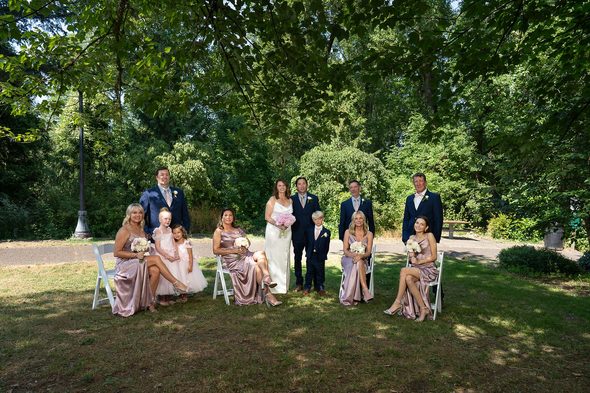 Wedding party posing under lush green trees at The Foundry.
