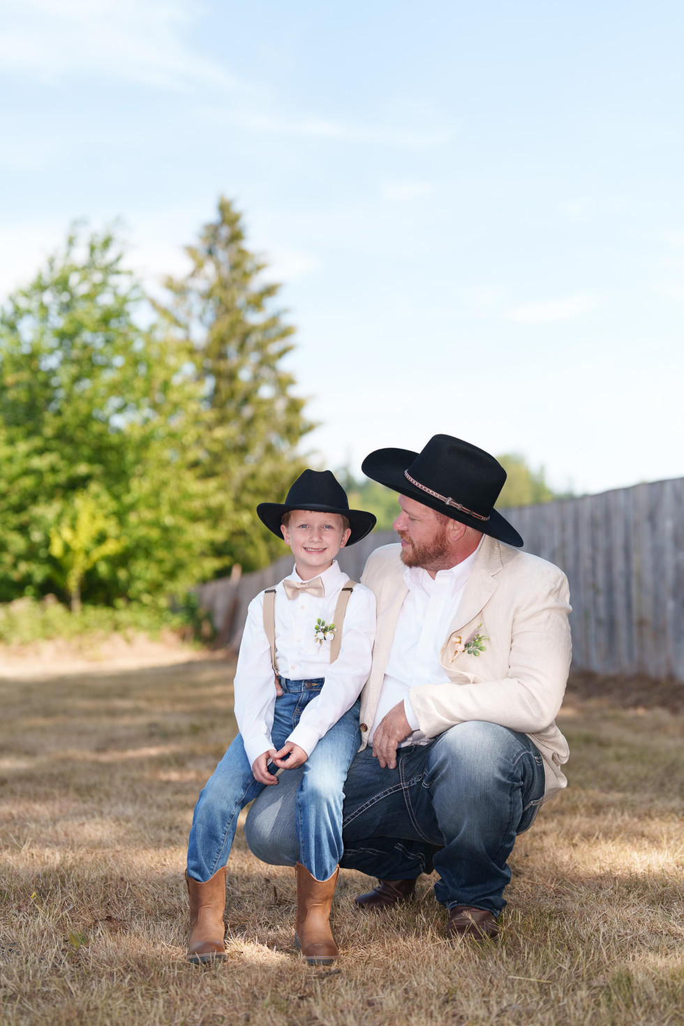 Man and boy in cowboy hats smiling outdoors at a wedding.
