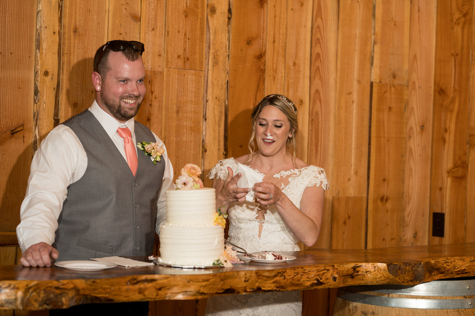 Bride with cake on her face, groom smiles at wedding reception.