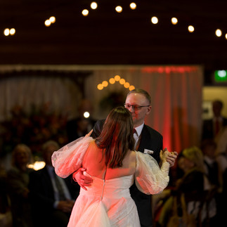 Couple dancing at a wedding reception with warm string lights overhead.