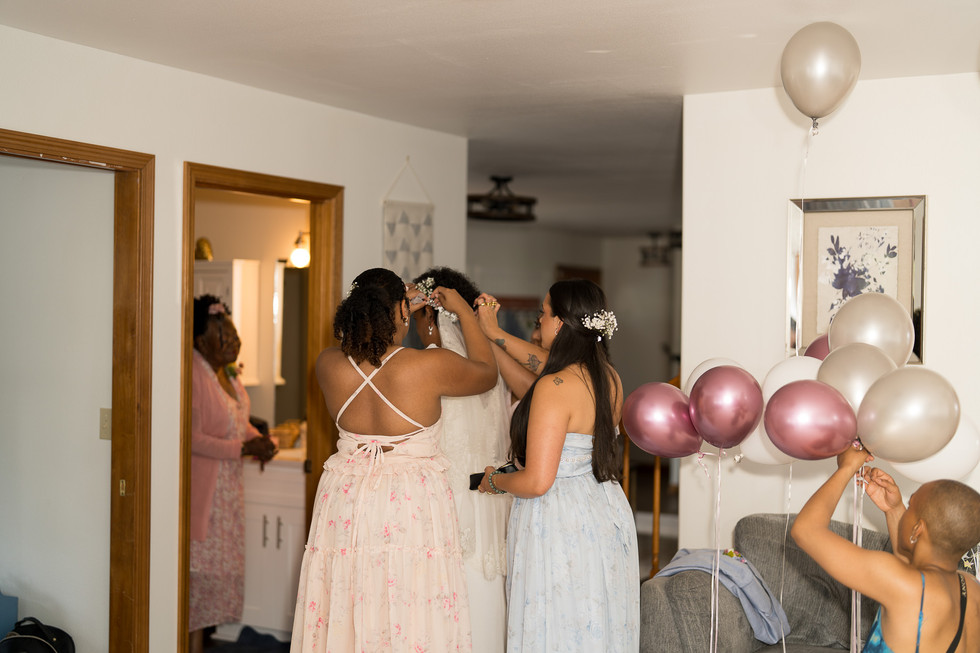 Bride being helped by bridesmaids with veil during wedding preparations.