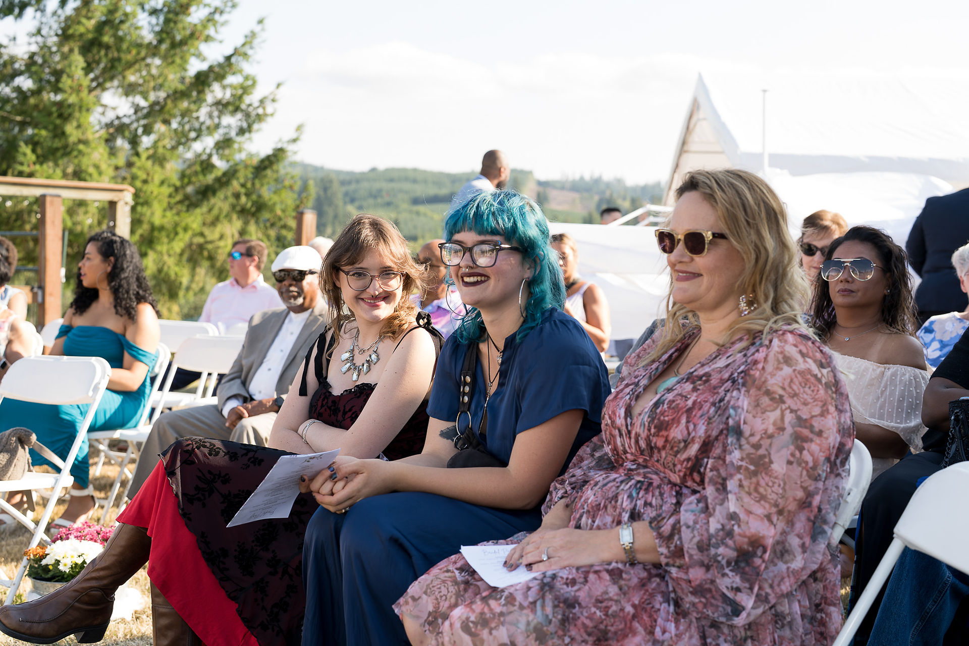 Happy guests smiling, seated outdoors at a sunny farm event.