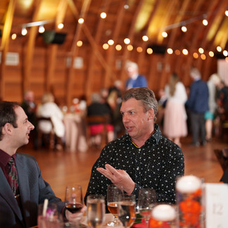 Two men intently conversing at a lively rustic wedding reception.