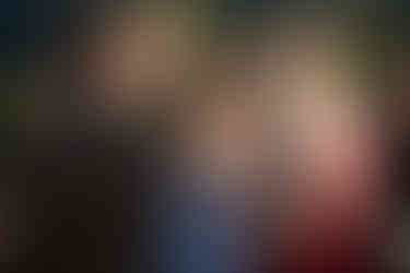 Woman in blue dress listening intently to two people talking outdoors.