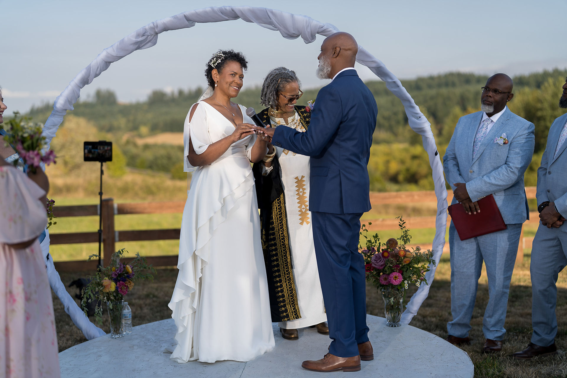 African American groom places ring on bride at intimate farm wedding.