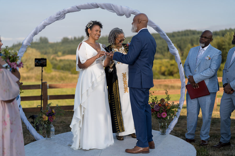 African American groom places ring on bride at intimate farm wedding.