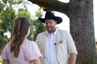 Man in cowboy hat smiling at woman during outdoor wedding ceremony.