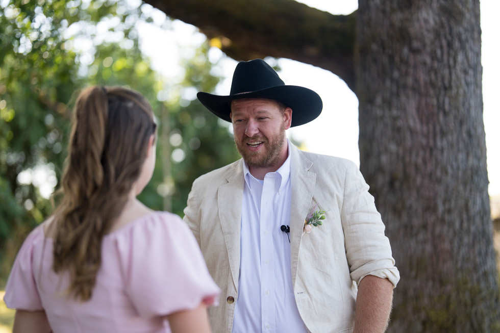 Man in cowboy hat smiling at woman during outdoor wedding ceremony.