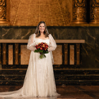 Bride in white wedding dress holding bouquet in ornate chapel background.