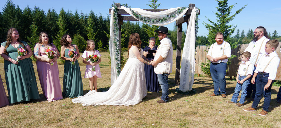 Bride and groom exchanging vows under an arbor on a sunny day.
