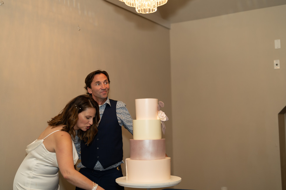 Bride blowing by groom next to elegant four-tier wedding cake.