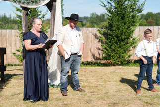 Woman officiating outdoor wedding ceremony for groom in cowboy hat.