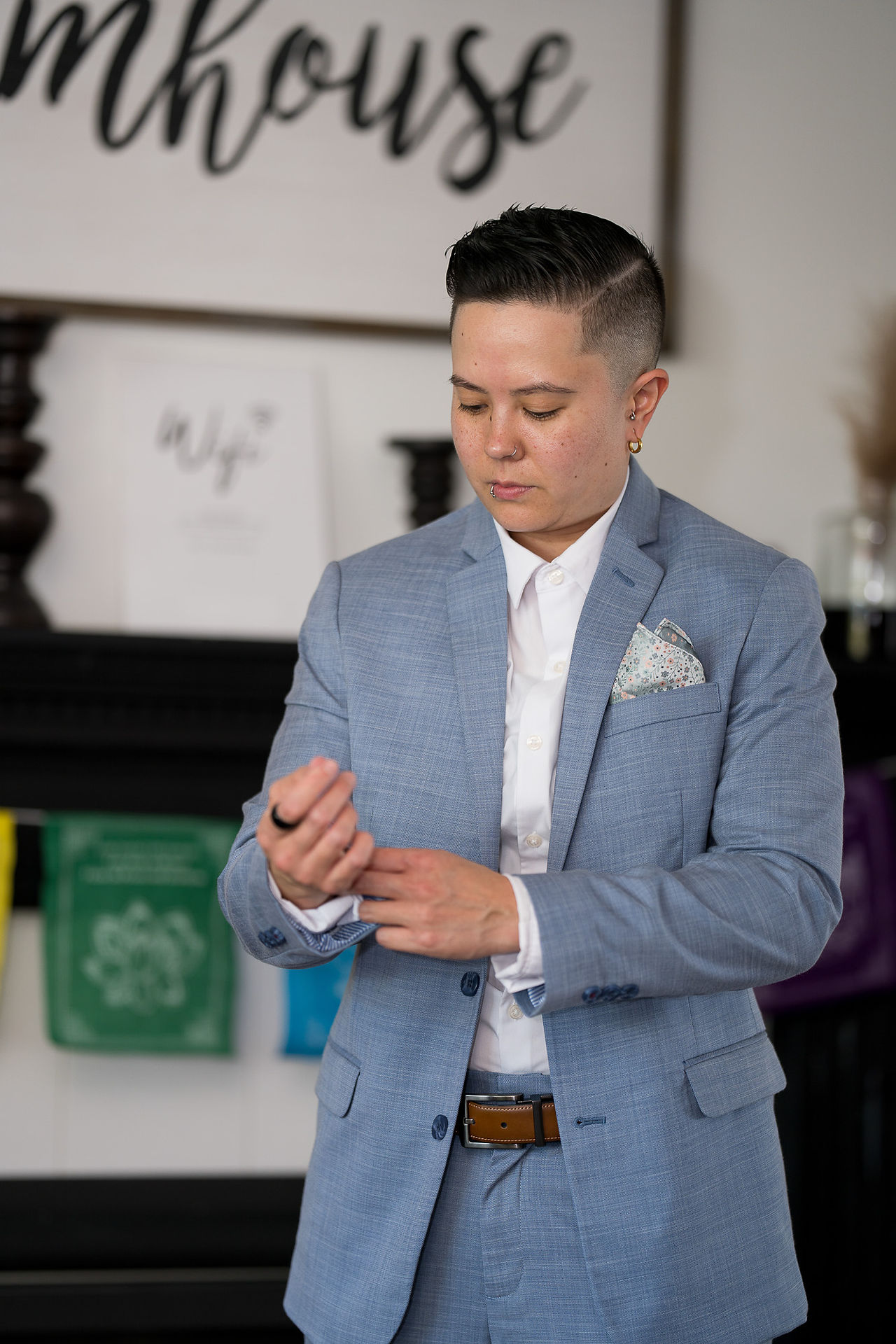 Person in light blue suit adjusts cuff, "Wife" sign visible behind.